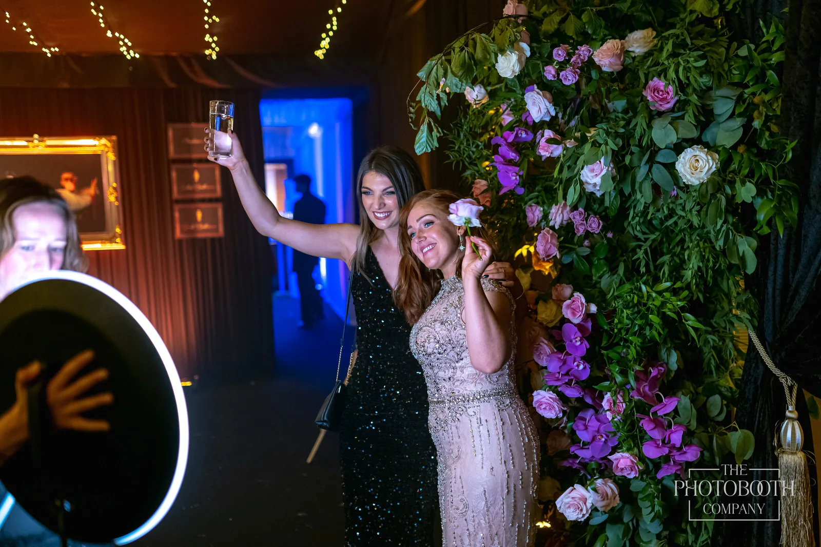 Roaming photo booth with a ring light capturing two guests toasting beside a floral wall at a corporate gala